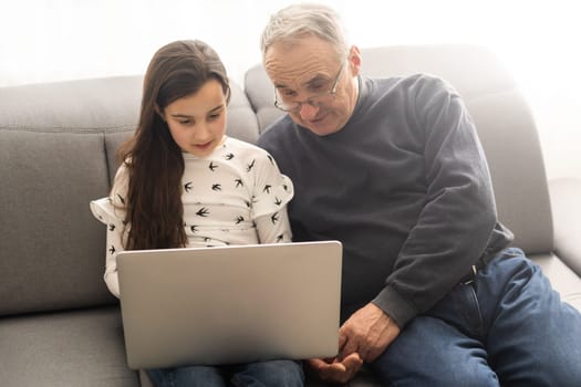 Happy retirement grandfather and pretty granddaughter laughing while watching e-book for learning to education together by laptop. Family educational at home concept. Technology and education