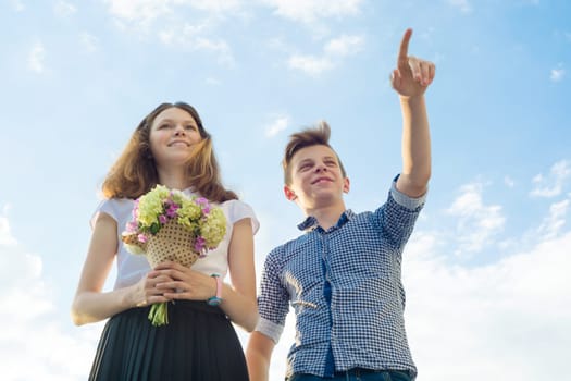 Happy couple of teens boy and girl 14, 15 years old. Young people smiling and talking, blue sky background.