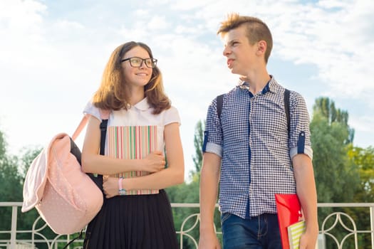 Adolescents students with backpacks, textbooks, go to school. Outdoor portrait of teenage boy and girl 14, 15 years old.