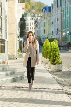 Young smiling woman walking on a city street, autumn sunny day.