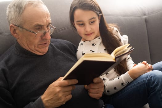 Happy little girl with grandfather reading story book at home.