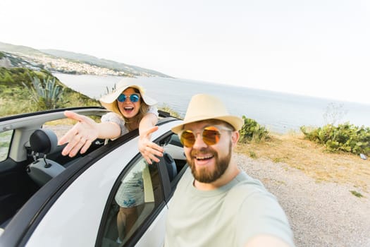 Happy beautiful couple in love taking a selfie portrait driving a convertible car on the road at vacation. Rental cars and vacation concept