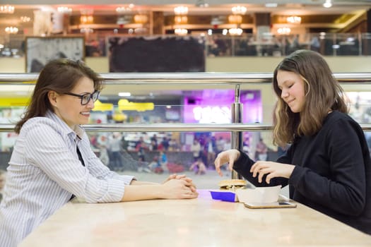 Communication of adult mother and teenage daughter. Background table in cafe, in the shopping mall entertainment center. Lifestyle, leisure and people concept