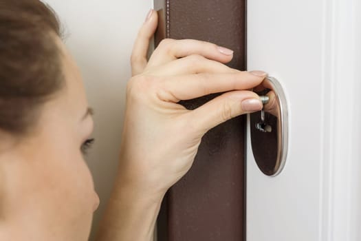 Woman peeks looks into the hole of the door lock.