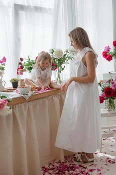 A little blonde girl with her mom on a kitchen countertop decorated with peonies. The concept of the relationship between mother and daughter. Spring atmosphere