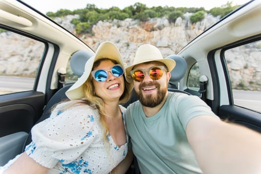 Romantic couple making selfie on smartphone camera in rental cabrio car on ocean or sea beach, enjoying summer vacation together and taking picture cellular resting near sea on weekends