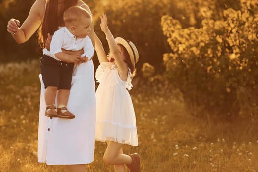 Happy family of mother, little son and daughter spending free time on the field at sunny day time of summer.