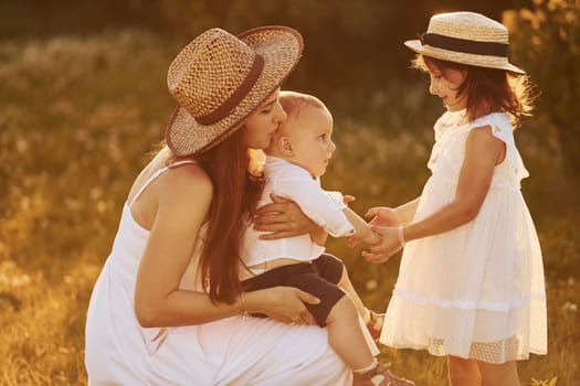 Happy family of mother, little son and daughter spending free time on the field at sunny day time of summer.