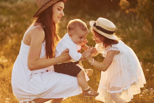 Happy family of mother, little son and daughter spending free time on the field at sunny day time of summer.