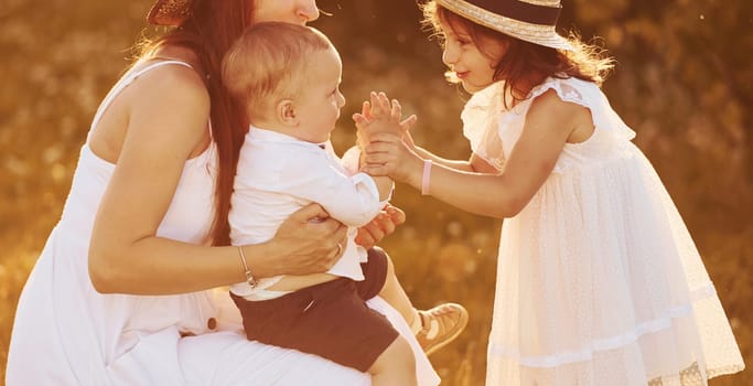 Happy family of mother, little son and daughter spending free time on the field at sunny day time of summer.