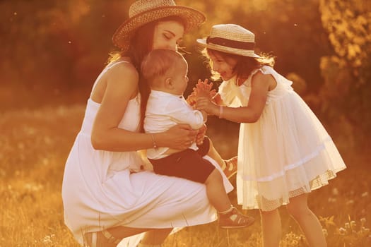 Happy family of mother, little son and daughter spending free time on the field at sunny day time of summer.