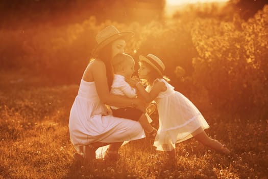 Happy family of mother, little son and daughter spending free time on the field at sunny day time of summer.