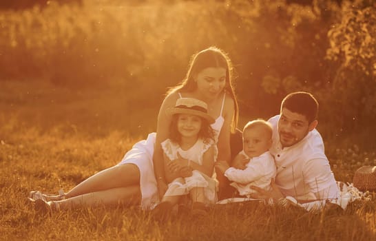 Sitting on the grass. Father, mother with daughter and son spending free time outdoors at sunny day time of summer.