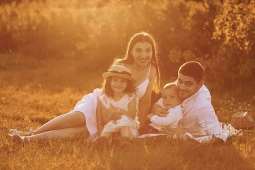 Sitting on the grass. Father, mother with daughter and son spending free time outdoors at sunny day time of summer.