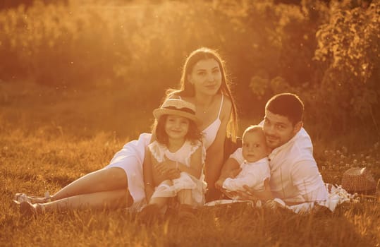 Sitting on the grass. Father, mother with daughter and son spending free time outdoors at sunny day time of summer.