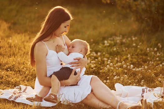 Happy mother breastfeeding her son on the field at sunny day time of summer.