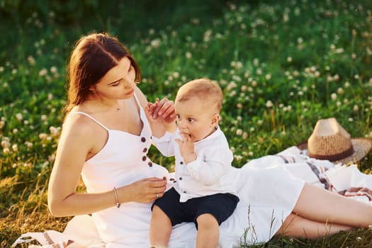 Happy mother with her son spending free time on the field at sunny day time of summer.