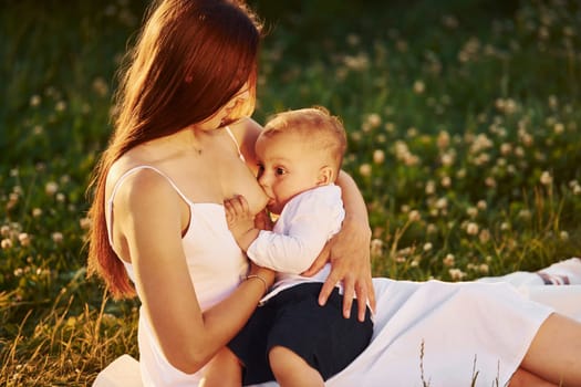 Happy mother breastfeeding her son on the field at sunny day time of summer.