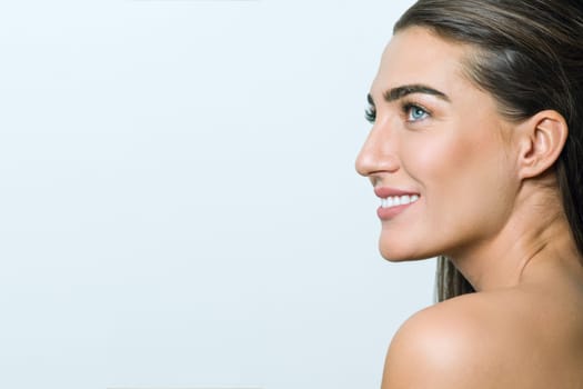 Smiling woman with clean skin, natural make-up, blue eyes, long straight healthy hair and white teeth on white background. Snapshot in profile, copy space