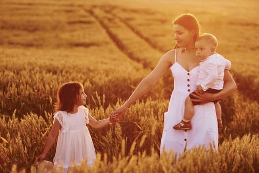 Cheerful family of mother, little son and daughter spending free time on the field at sunny day time of summer.