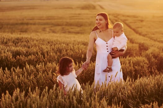 Cheerful family of mother, little son and daughter spending free time on the field at sunny day time of summer.