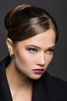 Beauty headshot portrait of a fashionable young woman with glamorous makeup and hairstyle, on a gray studio background