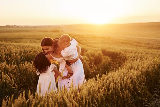 Cheerful family of mother, little son and daughter spending free time on the field at sunny day time of summer.