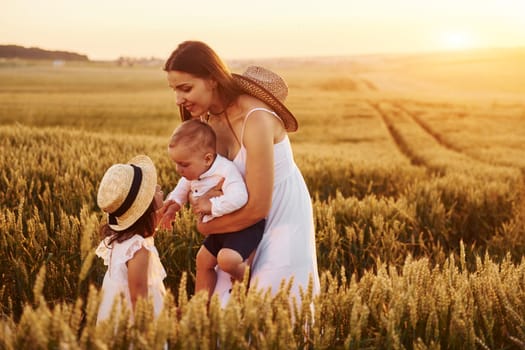 Cheerful family of mother, little son and daughter spending free time on the field at sunny day time of summer.