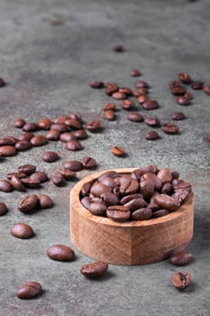 Roasted coffee beans in a wooden bowl and on the surface around. Selective focus.