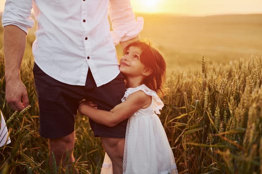 Girl embraces parent. Father with daughter spending free time on the field at sunny day time of summer.