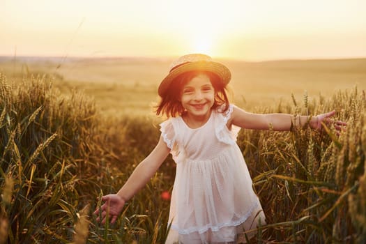 Cheerful little girl in white dress running in the agricultural field at summer day time.