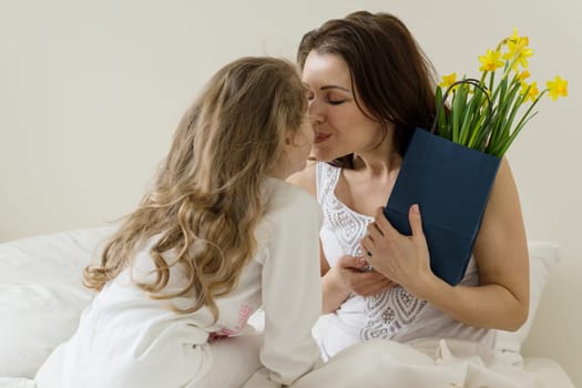 Mothers Day. Mother holds a bouquet of flowers kisses and hugs a little daughter. Background interior of bedroom, mother in bed, morning