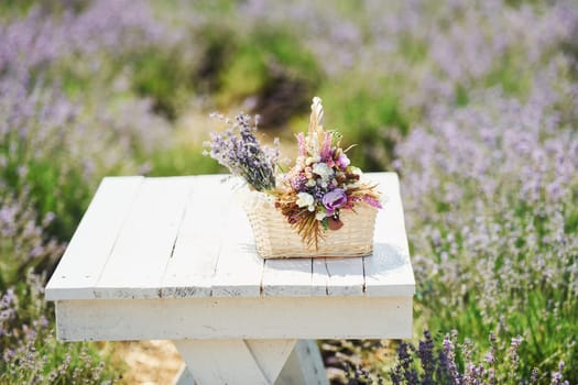 Close up view of bouquet of lavender flowers in basket that lying on the white table in field.