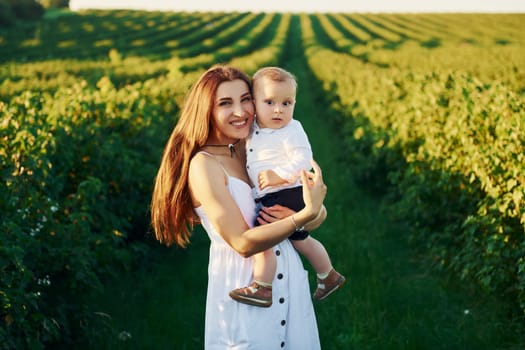 Positive mother with her son spending free time on the field at sunny day time of summer.