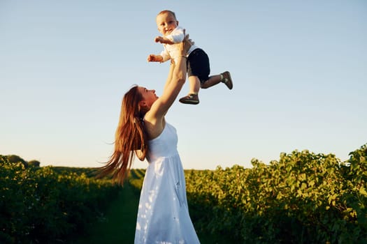 Positive mother with her son spending free time on the field at sunny day time of summer.