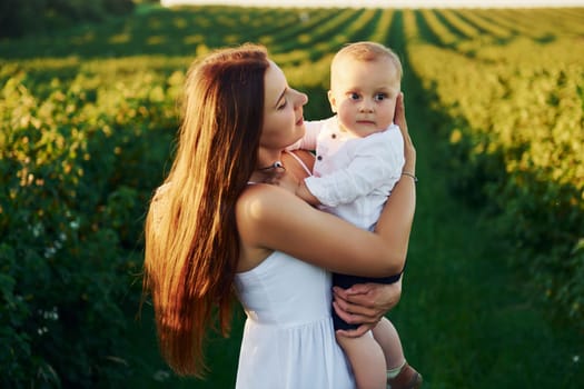 Positive mother with her son spending free time on the field at sunny day time of summer.