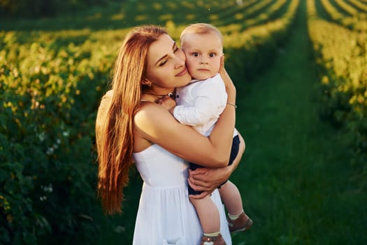 Positive mother with her son spending free time on the field at sunny day time of summer.