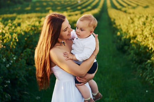 Positive mother with her son spending free time on the field at sunny day time of summer.