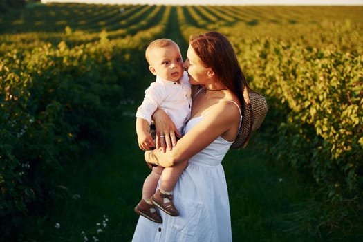 Positive mother with her son spending free time on the field at sunny day time of summer.