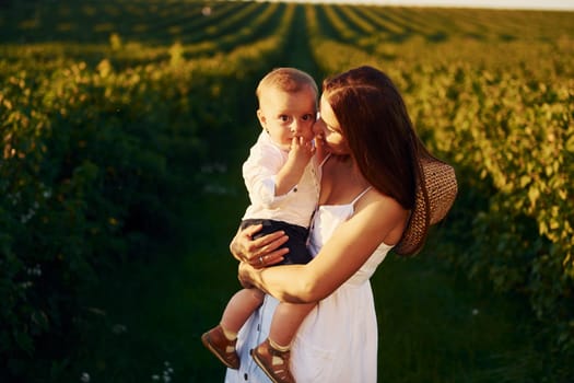 Positive mother with her son spending free time on the field at sunny day time of summer.