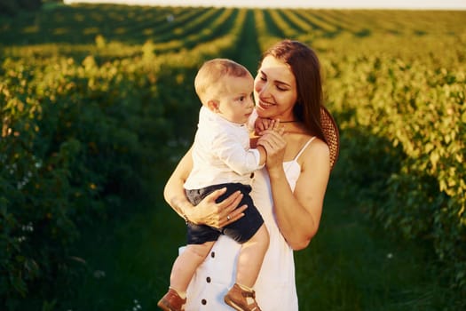 Positive mother with her son spending free time on the field at sunny day time of summer.