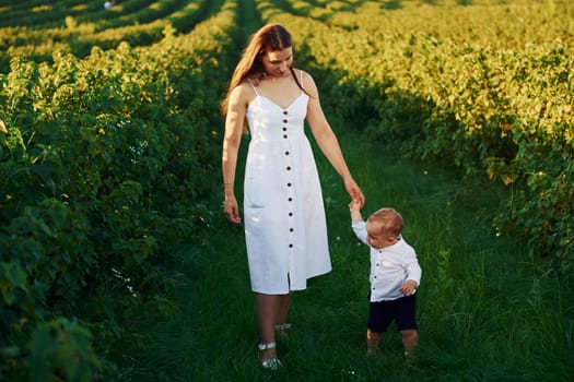 Positive mother with her son spending free time on the field at sunny day time of summer.