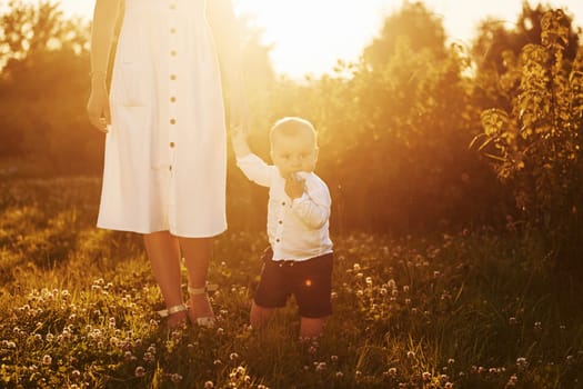 Positive mother with her son spending free time on the field at sunny day time of summer.