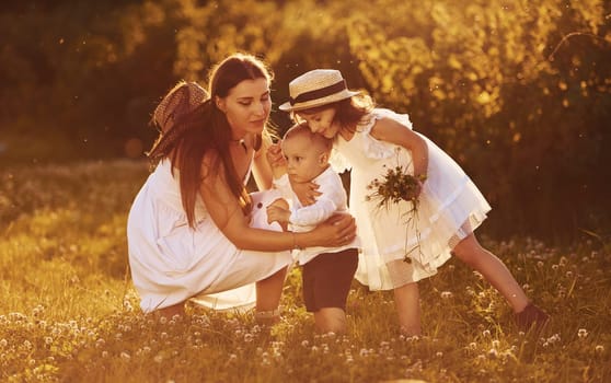 Cheerful family of mother, little son and daughter spending free time on the field at sunny day time of summer.