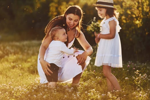 Happy family of mother, little son and daughter spending free time on the meadow at sunny day time of summer.