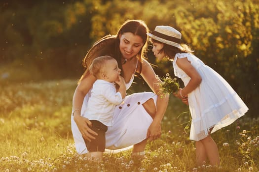 Happy family of mother, little son and daughter spending free time on the meadow at sunny day time of summer.