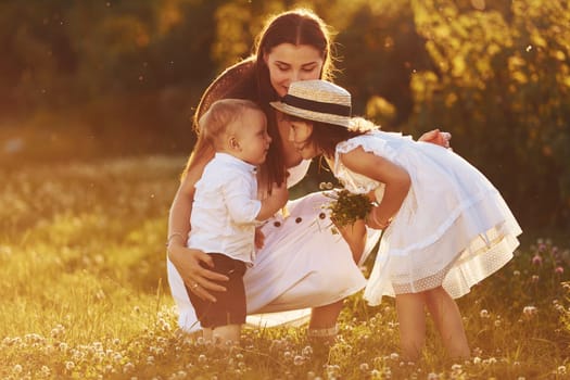 Happy family of mother, little son and daughter spending free time on the meadow at sunny day time of summer.