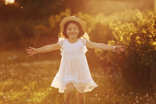 Happy little girl in white dress have fun outdoors on meadow at summertime.