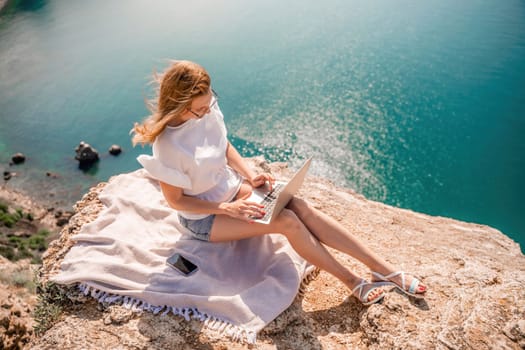 Freelance women sea working on the computer. Good looking middle aged woman typing on a laptop keyboard outdoors with a beautiful sea view. The concept of remote work