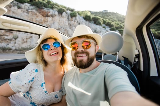 Romantic couple making selfie on smartphone camera in rental cabrio car on ocean or sea beach, enjoying summer vacation together and taking picture cellular resting near sea on weekends